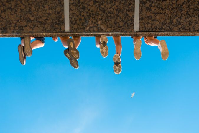 Low-angle view of people's legs dangling from bridge