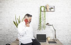 Side view of middle aged man talking on the phone and working in office
