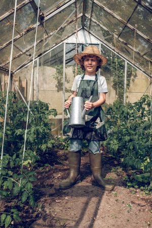 Cheerful preteen boy with watering can in glasshouse