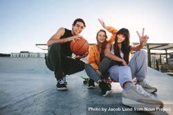 Group of friends sitting at skate park with skateboard and basketball 0LrKA4