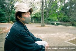 Man with beige hat and gray facemask sitting at a park 41APN4