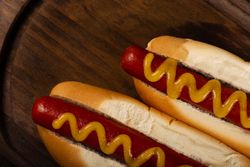 Top view of two hot dogs with mustard on wooden board