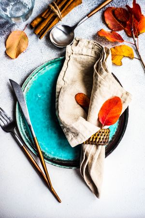 Autumn place setting with colorful leaves and cinnamon sticks garnishing teal plate