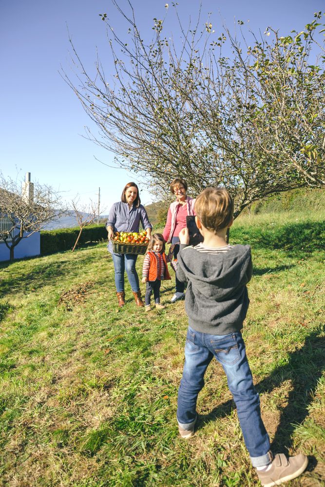 Boy taking photo to family with freshly picked apples in basket