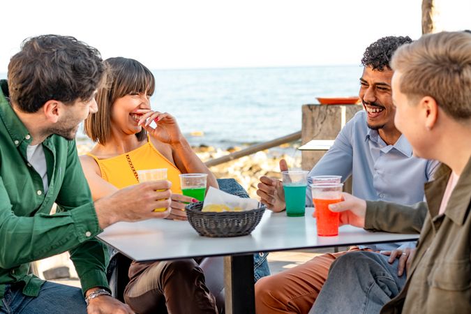 Happy friends sharing laughter and colorful drinks by the seaside