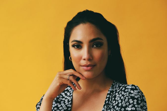 Headshot of serious Hispanic woman looking at camera in yellow room, copy space