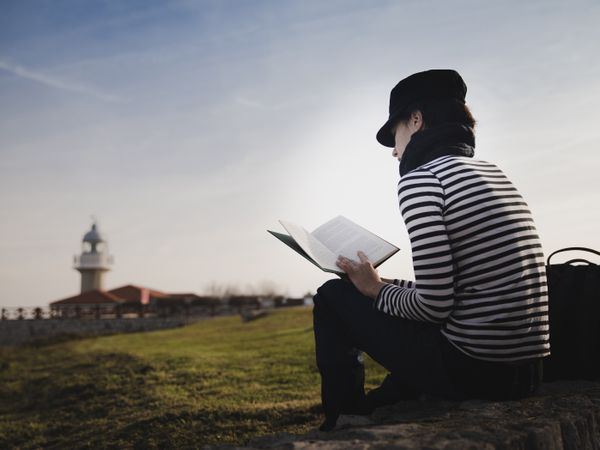 Woman with book on grass near lighthouse
