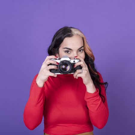 Woman taking a photo with her film camera over a violet background.