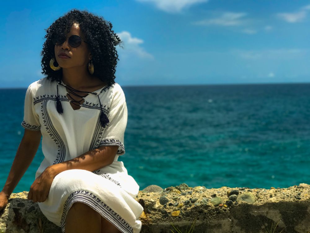 Black woman in light dress sitting on balustrade against the sea view