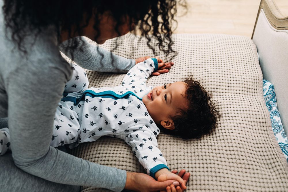 Cute baby boy lying down looking up at mother holding his hands