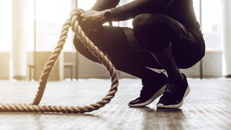 Close up of a man sitting on his toes holding a pair of battle ropes for workout