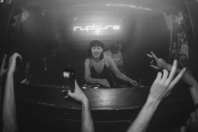 Female DJ spins records at Rupture night club as audience raises hands
