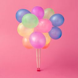 Doll legs with colorful balloons on pastel pink background
