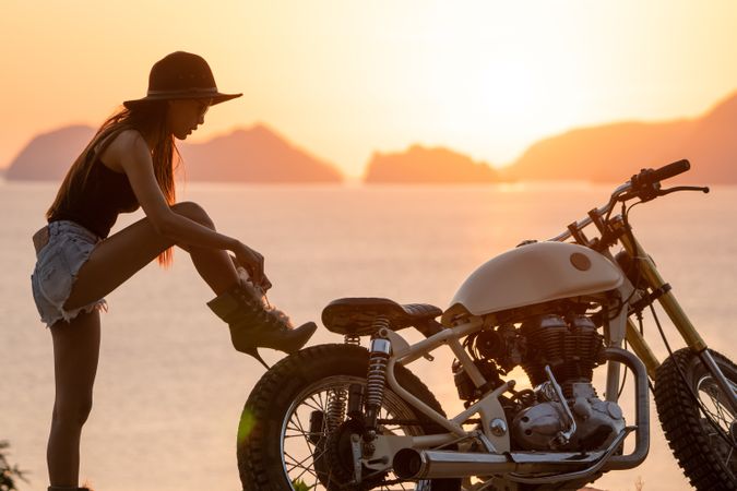 Woman tying boots near motorcycle
