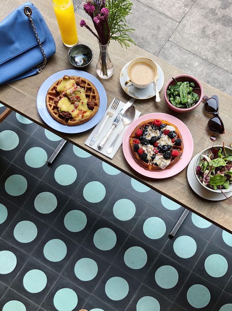 Top view of two waffle plates and salad beside cup of coffee and orange juice at a restaurant