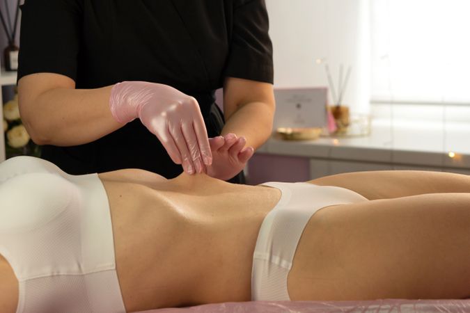 Therapist performs abdominal massage in spa treatment room setting.