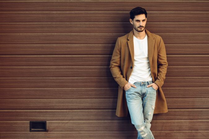 Man leaning on brown wall in winter coat