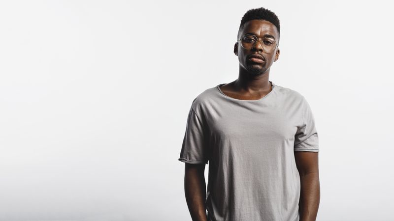 Black male in eyeglasses and tshirt standing against neutral background
