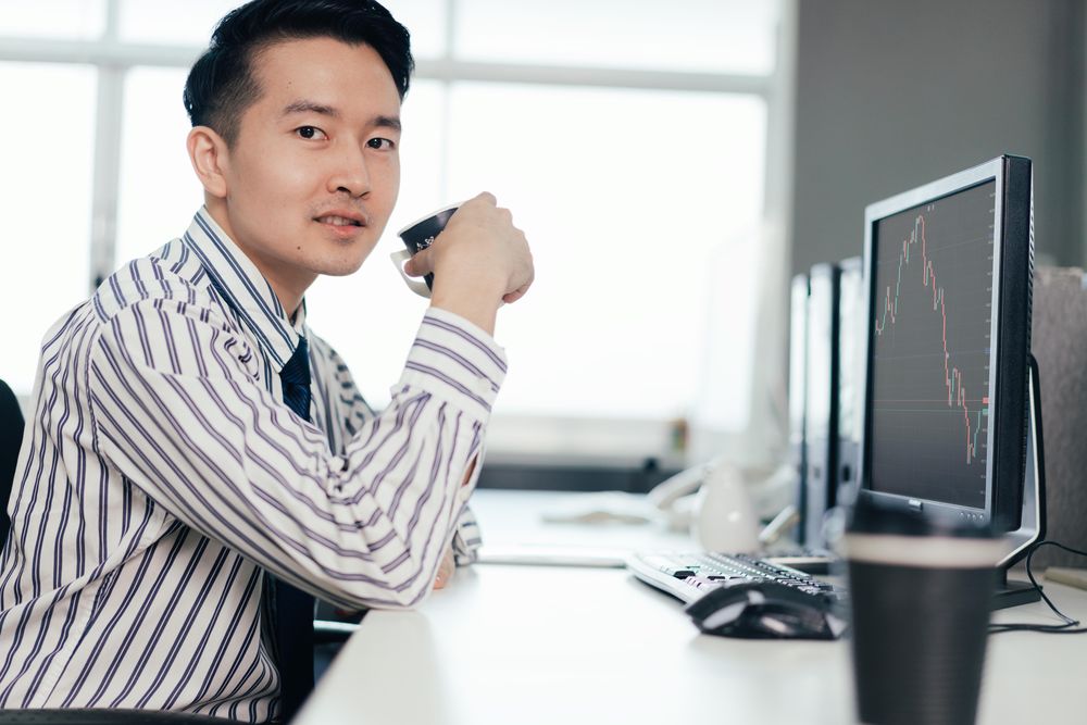 Man at work drinking coffee in front of data on computer screen