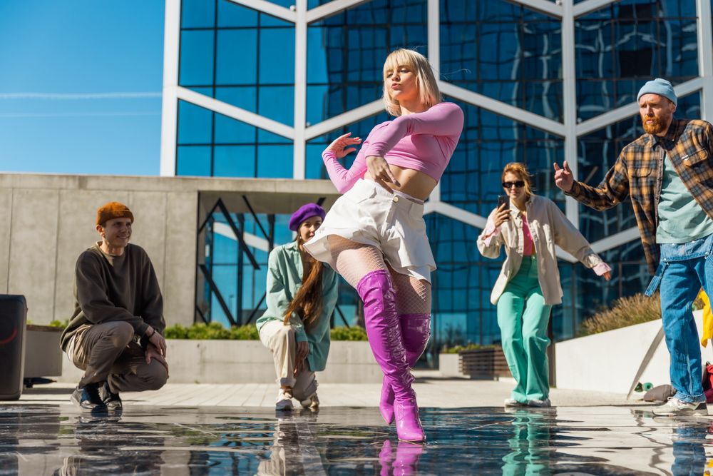 Vibrant Outdoor Scene Capturing A Diverse Group Of Young Adults Dancing Joyfully In Front Of A Modern Glass Building