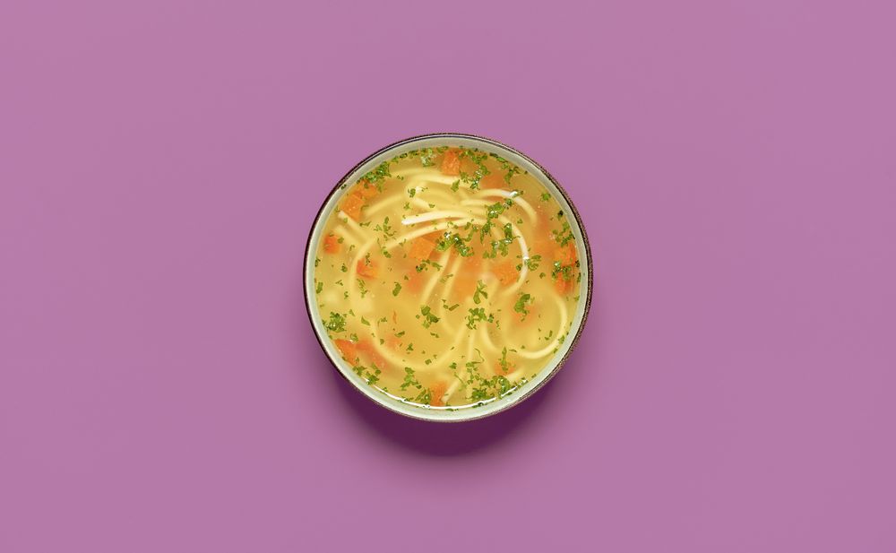 Chicken noodle soup bowl top view on a colored table