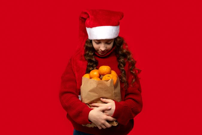 Girl in Santa hat looks down at bag with oranges.
