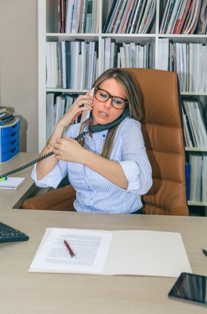 Busy businesswoman talking with cell and land line phone in office