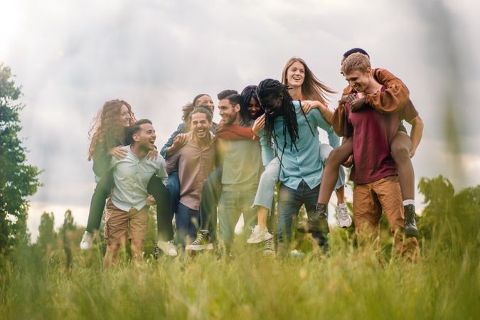 Friends piggybacking in park, seen from long grass