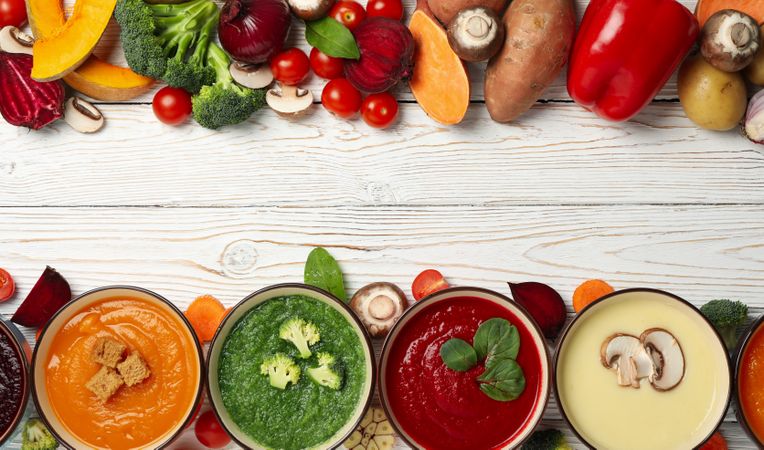 Line of soups and vegetables with copy space on wooden table