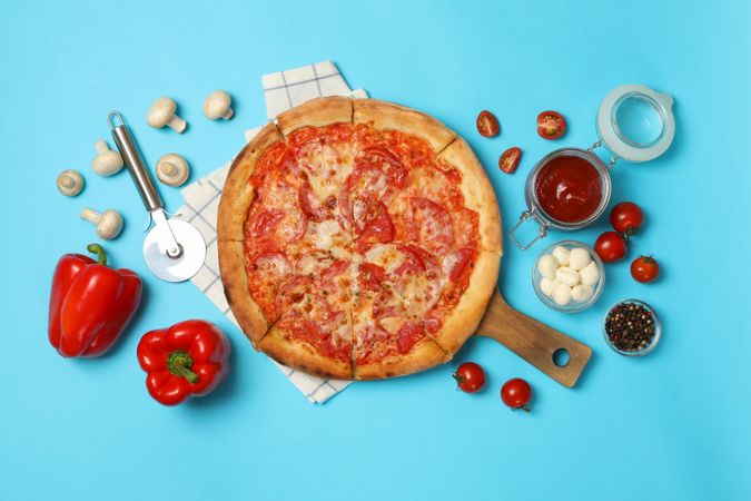 Tasty pizza and ingredients on blue background
