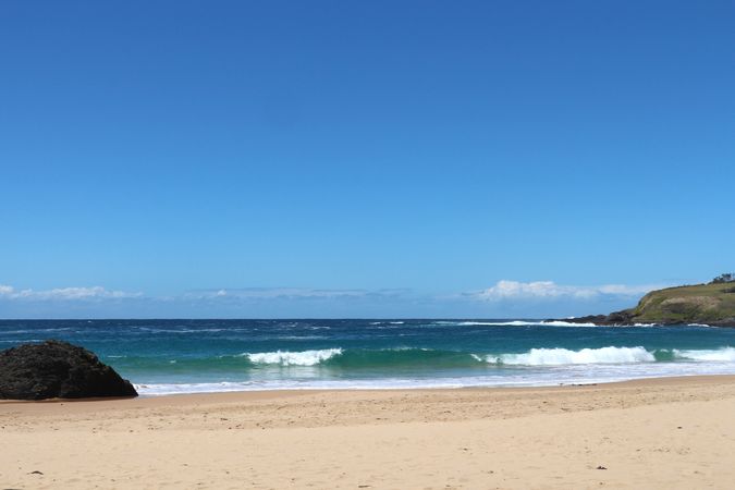 Vibrant beach view with rolling waves and clear skies during midday by the shore