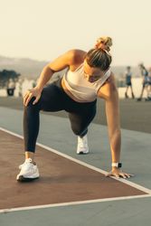 Focused athlete woman in a runner's lunge pose stretching on a track during an outdoor workout