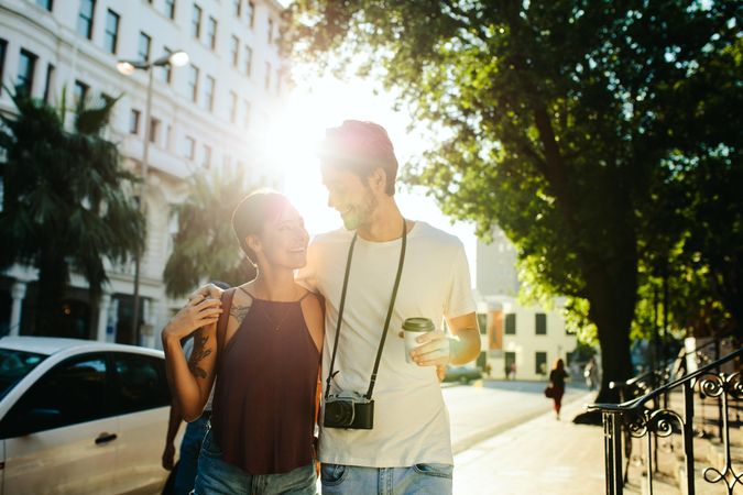 Happy tourist couple walking in the street holding a coffee cup with sun in the background