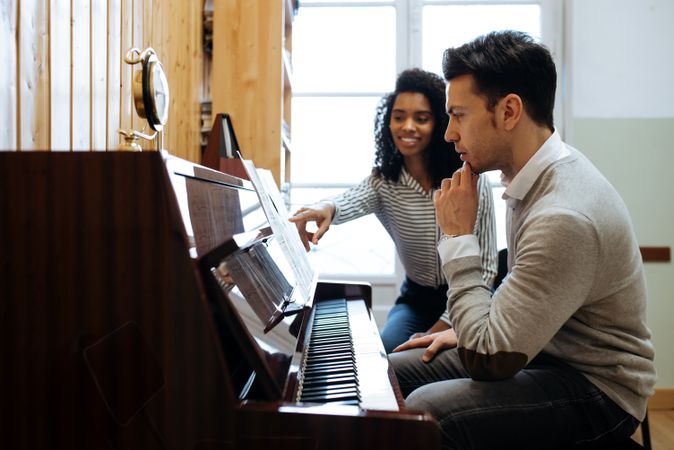 Man playing piano near woman teaching in studio