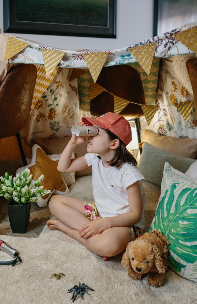 Girl playing with cardboard binoculars while camping at home
