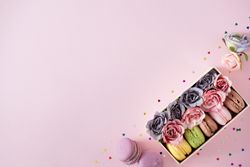 Box of macarons and flowers on pink background
