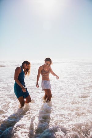 Two young women walk at the edge of the water at the beach