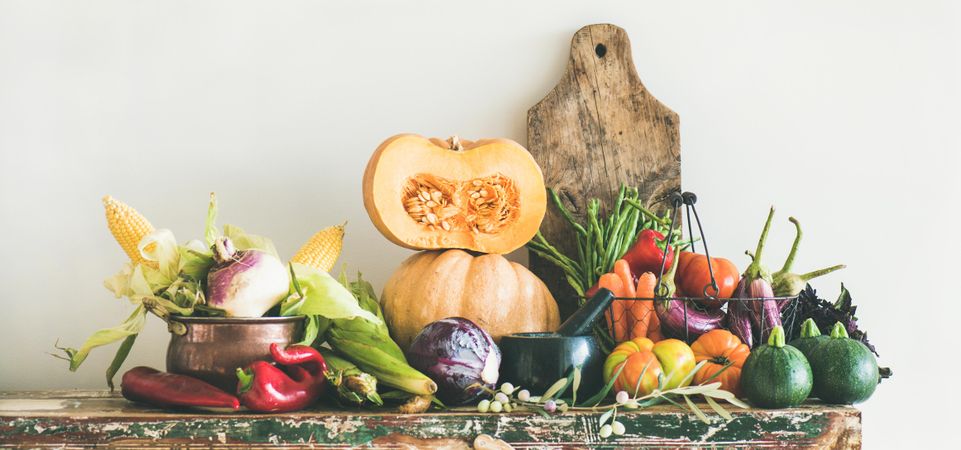 Fresh autumnal produce on kitchen counter, with halved squash and wooden board