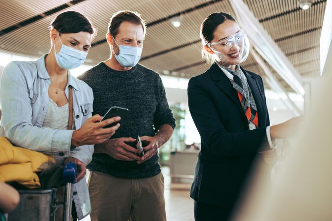 Male and female tourists in face masks helped by ground attendant at airport