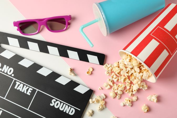 Bucket with popcorn, clapperboard, drink and 3d glasses on two tone background