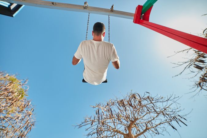 Man swinging on playground in sunlight