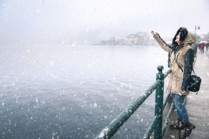 Woman reaching for snowflakes on a snowy day by a lake