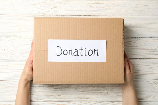 Female hands hold paper box with text Donation on wooden background