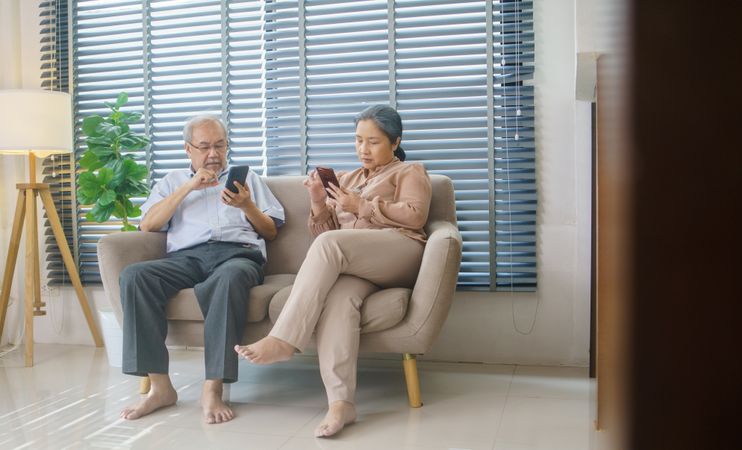 Older man and woman using smartphones on couch