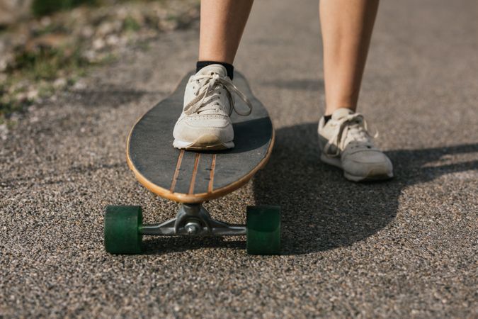 Anonymous woman riding longboard on asphalt road