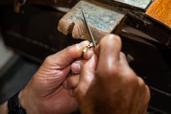 Goldsmith working and creating in his crafting gold jewelry workshop. Jeweler liming a silver jewel.