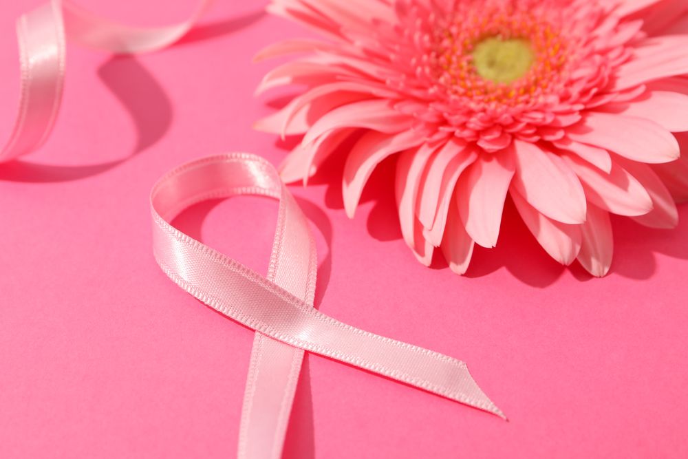 Pink awareness ribbon and gerbera on color background, space for text.