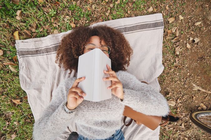 Black woman hiding face behind book in nature