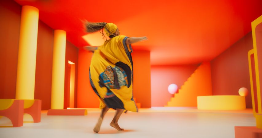 Black Woman in African Outfit Dancing Energetically in Geometric Abstract Orange Environment. Creative Female Performing Dance Choreography in Studio, Making Moves, Having Fun, Practicing
