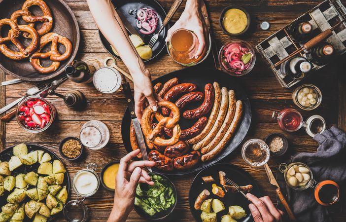 German sausages and pretzels displayed on wooden table with hands holding beer and pretzel